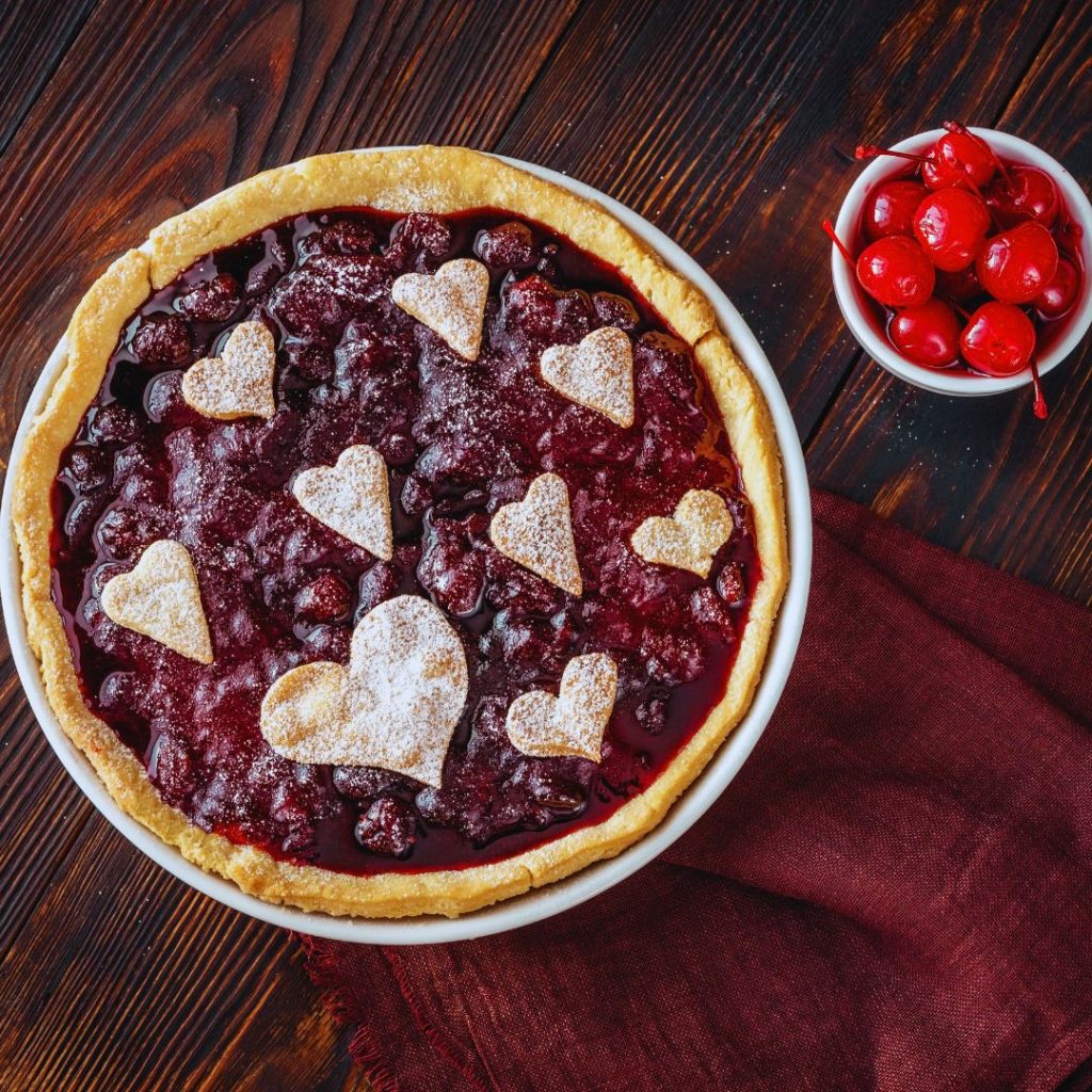 cherry tart with heart shapes on the top made out of crust and a bowl of cherries sitting nearby